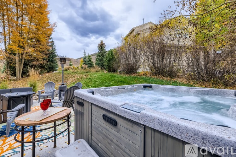 A hot tub is surrounded by chairs and a table with a glass of wine on it.