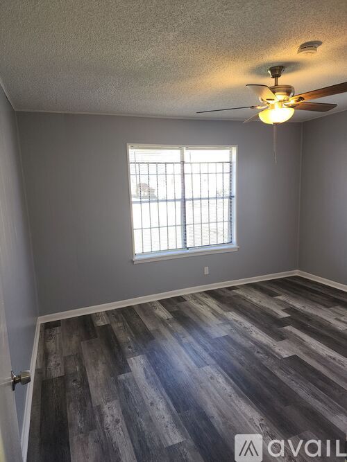 A room with a ceiling fan and a window with bars.