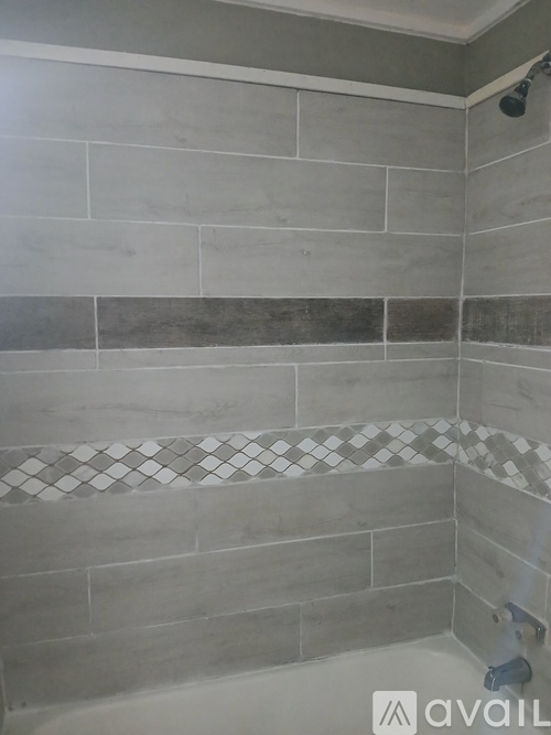 A shower area with grey tiles and a white shower head.