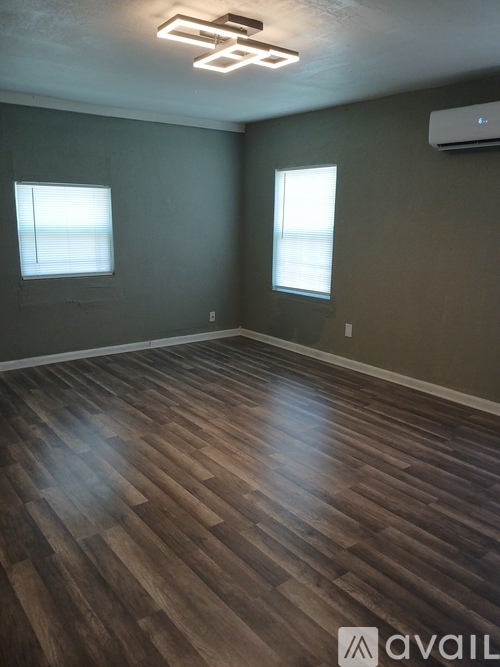 A room with wooden flooring and two windows.