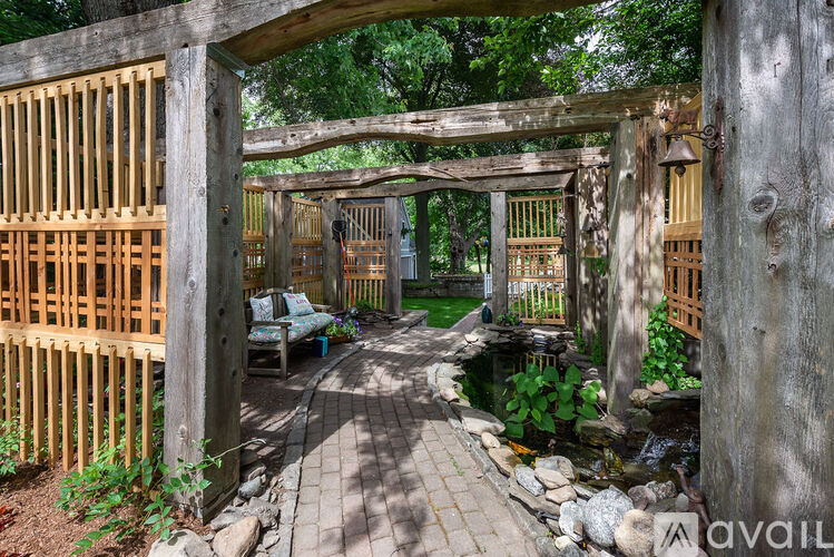 A wooden gate leads to a garden with a bench and a water feature.