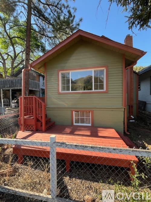 A green house with a red deck and a red chair.
