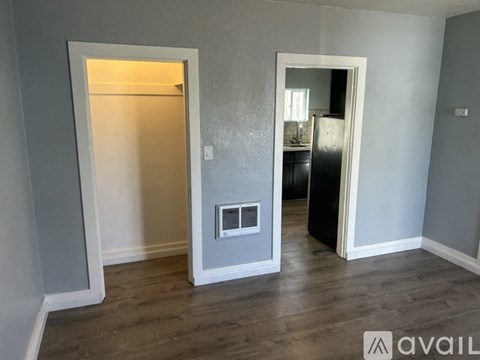 A room with a doorway leading to another room and a refrigerator in the corner.