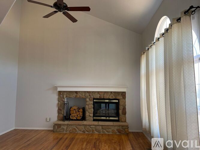 A living room with a stone fireplace and a fan on the ceiling.