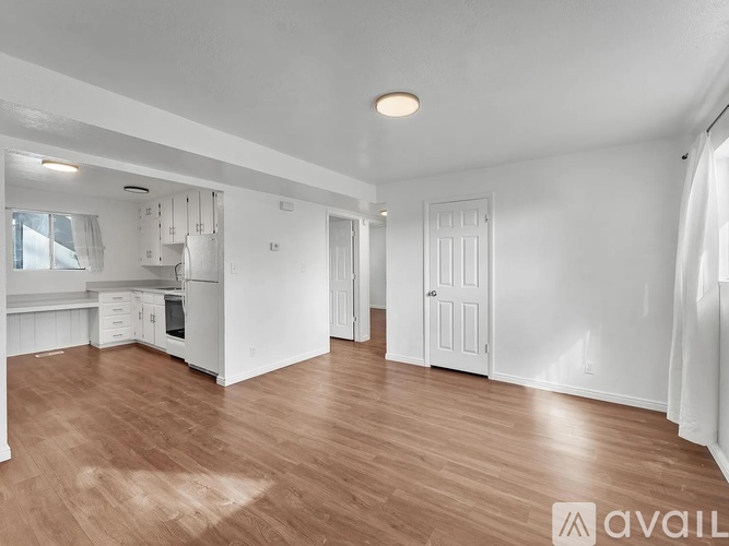 A spacious kitchen and living room with wooden floors and white walls.