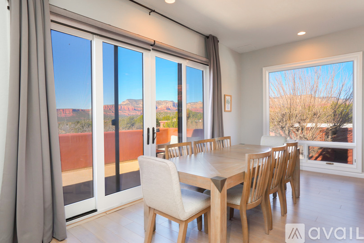 A dining room with a table and chairs and a view of the outdoors through the windows.