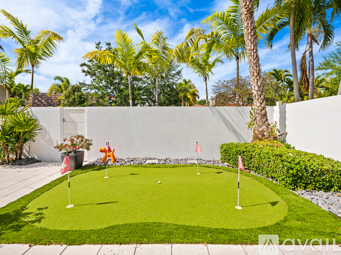 A small putting green surrounded by a white wall and palm trees.