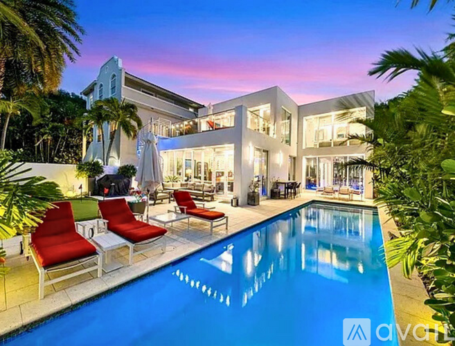 A modern house with a pool and red chairs.