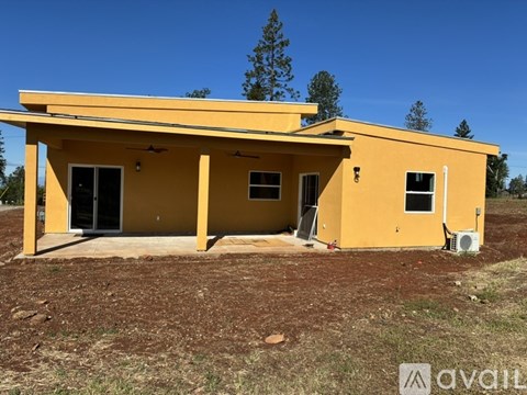 A yellow house with a brown roof and a tree in the background.
