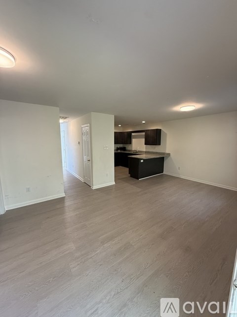 A spacious room with light wood flooring and white walls.