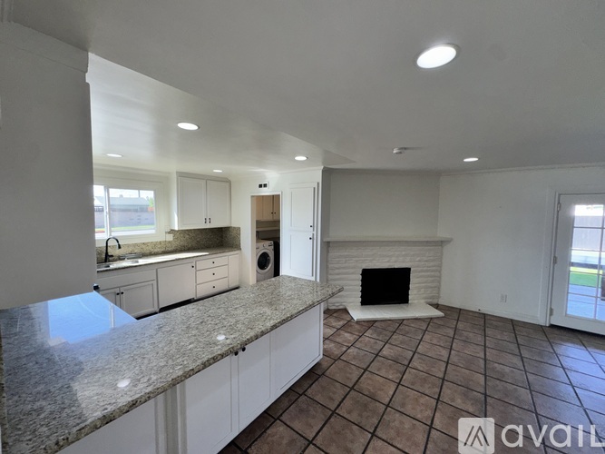 A large, empty living room with a fireplace and a kitchen area in the background.