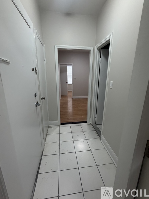 A hallway with white walls and tile flooring leading to a door.