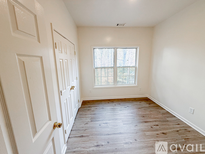 A room with a white door and a window with a view of trees.