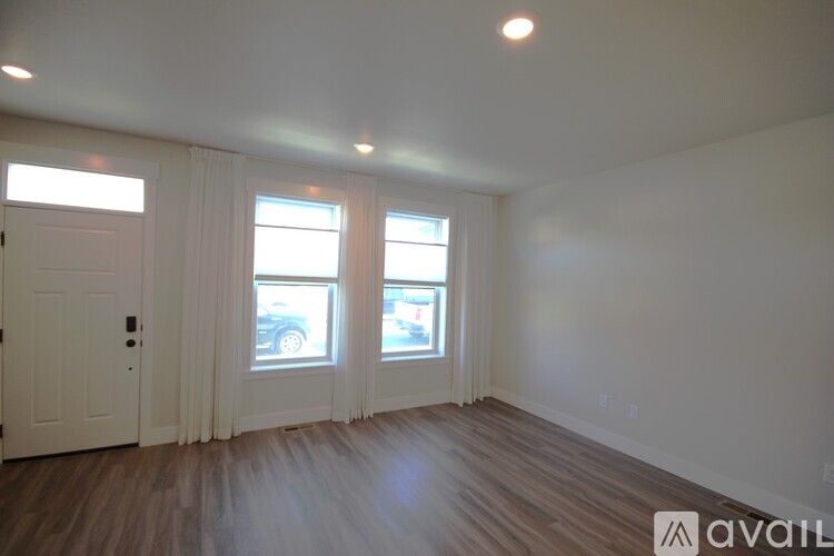 A room with wooden floors and white walls, with a door and two windows.