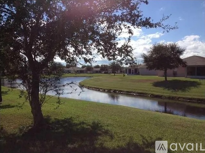 A tree stands in front of a house with a pond in the foreground.