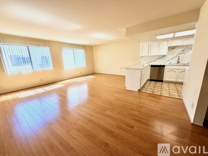 A spacious room with wooden flooring and a kitchen area in the background.