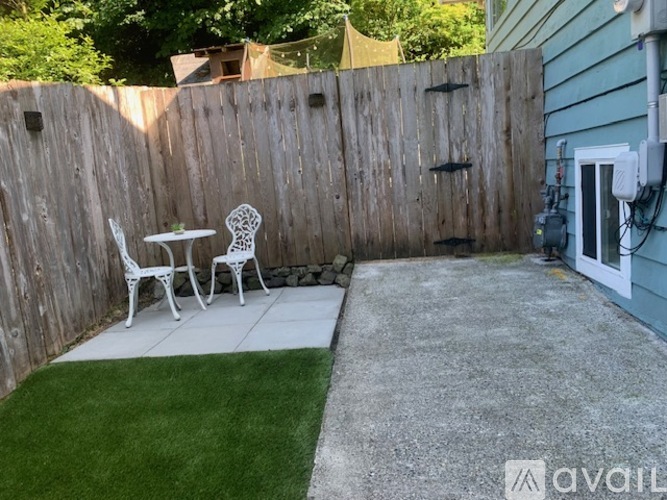A backyard with a wooden fence, a small table and two chairs, and a concrete patio.