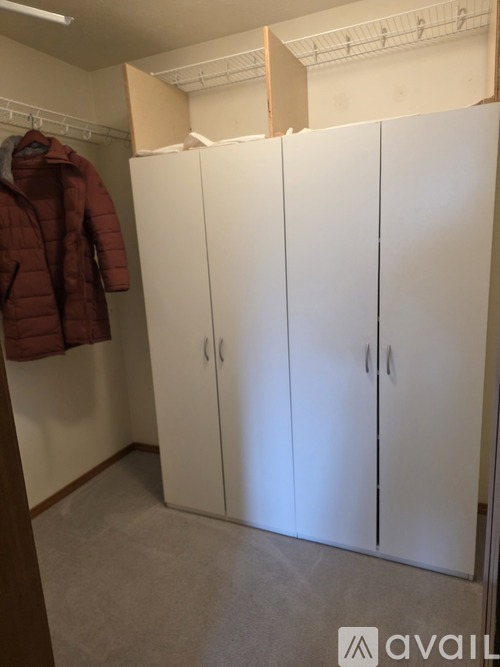 A room with a red jacket hanging on a hanger and a white wardrobe.