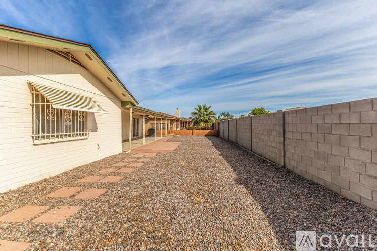 A long, narrow driveway with a gravel surface leads to a white building with a metal awning.