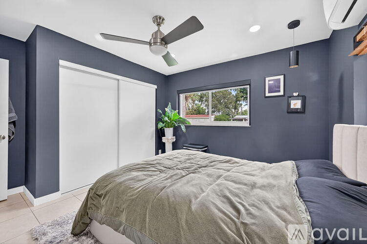 A bedroom with a bed, a ceiling fan, and a window with a view of the outside.