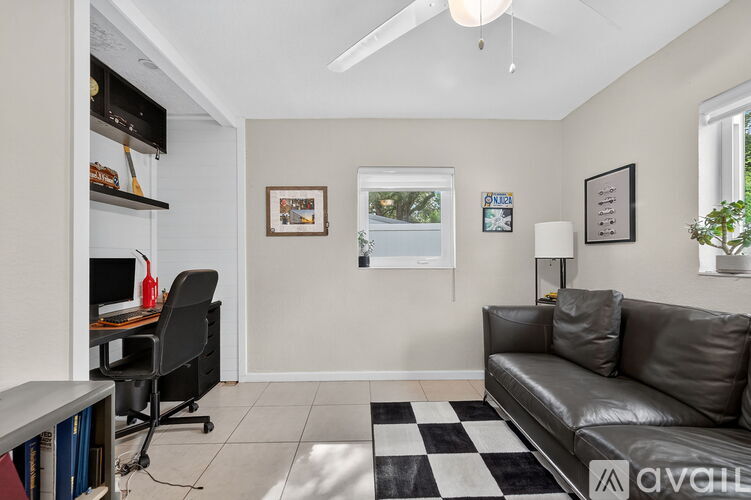 A black leather couch sits in a living room with a checkered rug in front of it.