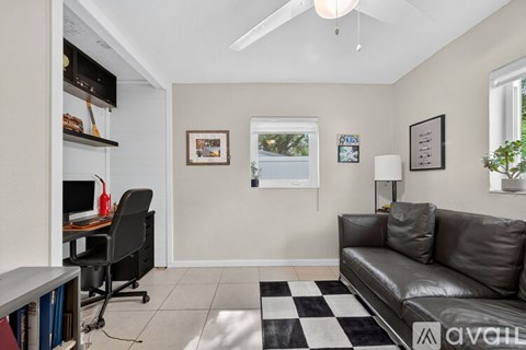 A black leather couch sits in a living room with a checkered rug in front of it.