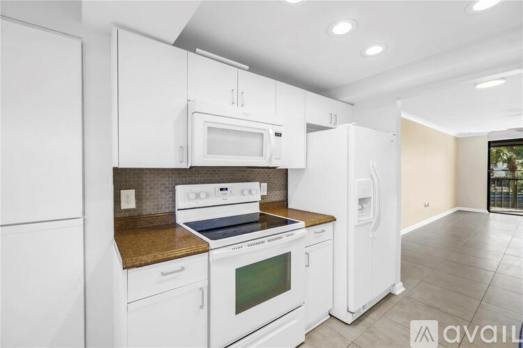 A kitchen with white cabinets and appliances, a countertop with a backsplash, and a window with a view of trees.
