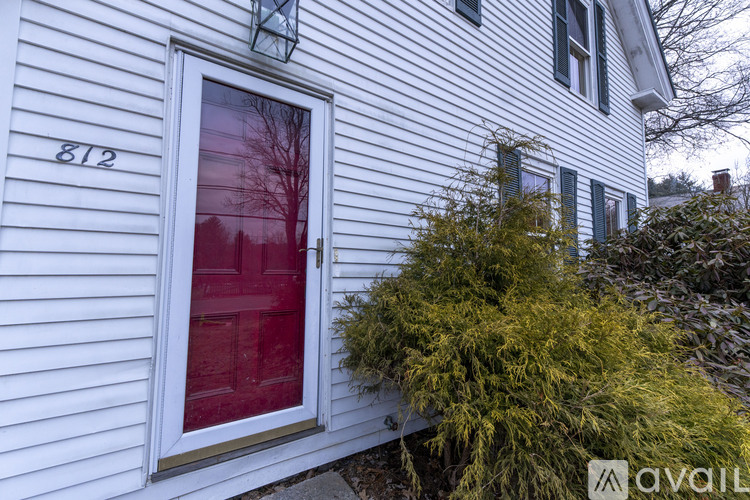 A white house with a red door and a window with a tree in front.
