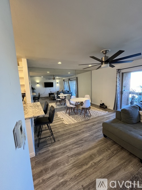 A living room with a grey couch, a dining table with chairs, and a ceiling fan.