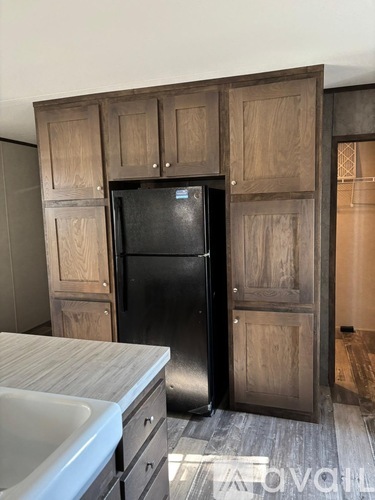 A black refrigerator is in a kitchen with wooden cabinets.