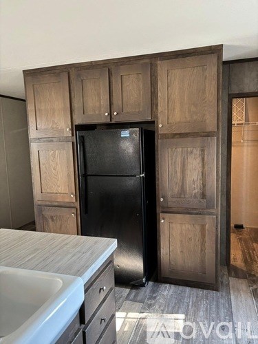 A black refrigerator is in a kitchen with wooden cabinets.