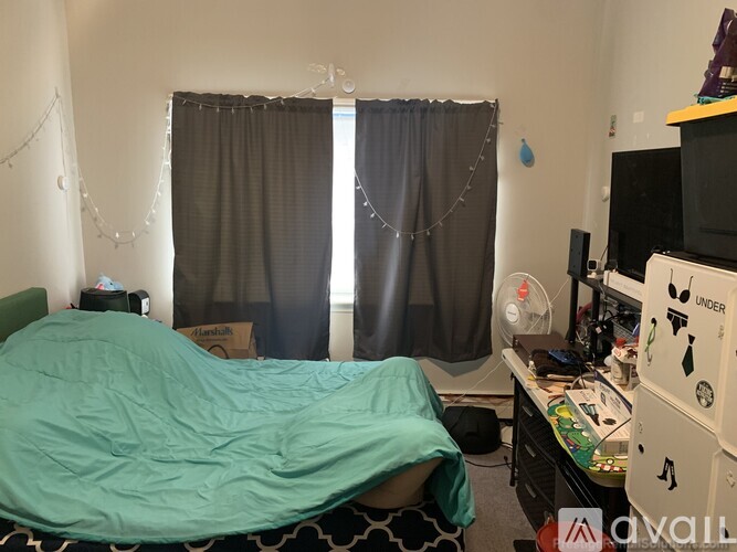A bedroom with a bed covered in a green blanket, a desk with a computer and a television.