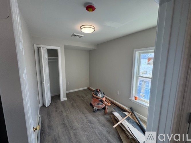 A room with a smoke detector on the ceiling and a window with a view of a construction site.