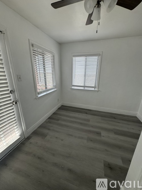 A room with a ceiling fan and two windows with blinds.