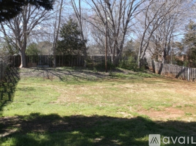 A grassy field with trees and a fence in the background.