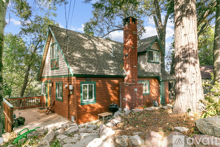 A house with a red brick chimney and a green roof is surrounded by trees.