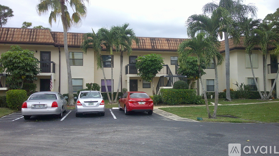 A red car is parked in a parking lot in front of a building with palm trees.