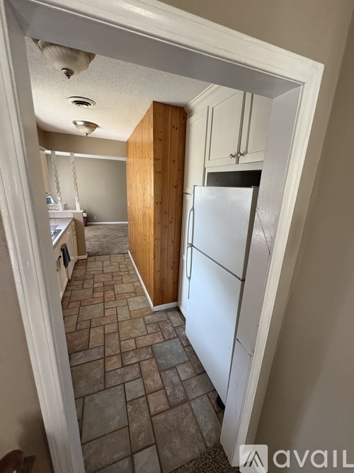 A kitchen with a refrigerator, wooden cabinets, and a tiled floor.