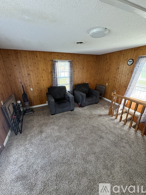 A living room with a grey carpet and wooden walls.