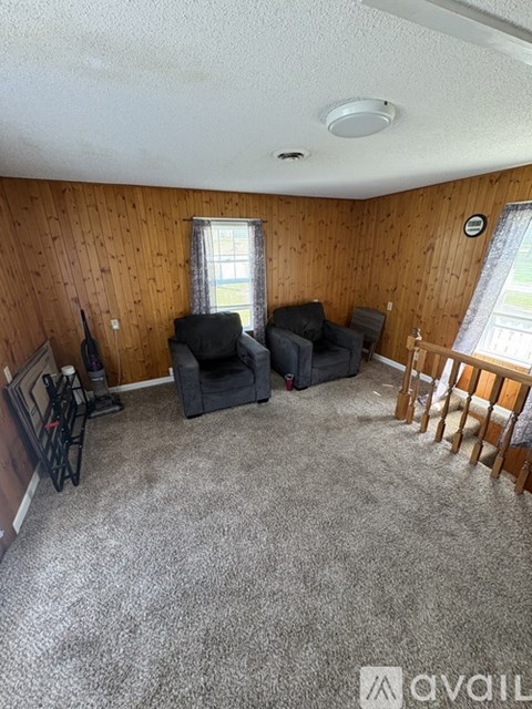 A living room with a grey carpet and wooden walls.