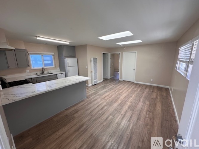 A spacious room with wooden flooring and a kitchen area with a countertop and cabinets.