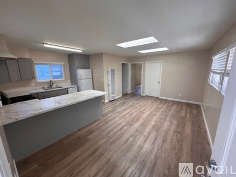 A spacious room with wooden flooring and a kitchen area with a countertop and cabinets.