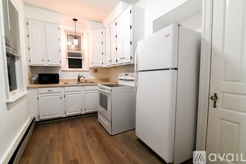 A kitchen with white cabinets and appliances, a wooden floor, and a door on the right.