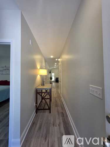A hallway with a lamp and a bed in the background.