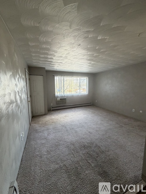 A room with a carpeted floor and a window with blinds.