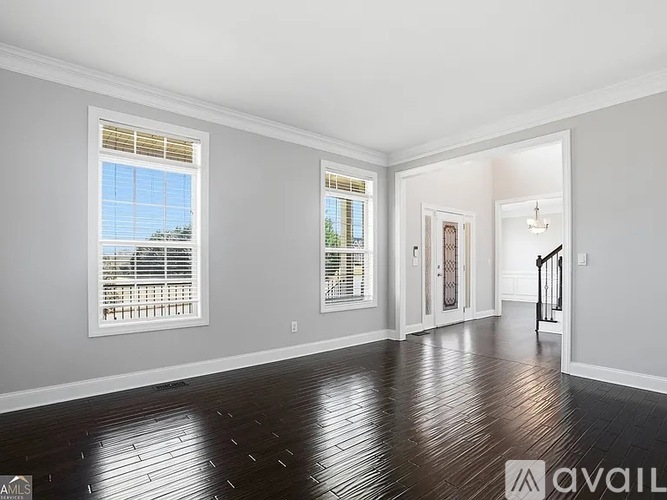 A spacious room with wooden flooring and two windows with blinds.