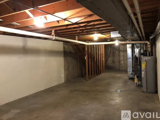 A spacious basement with a concrete floor and walls, wooden beams on the ceiling, and a few pieces of construction equipment.