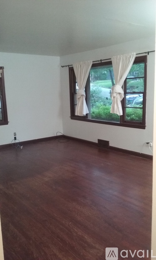 A room with wooden floors and a window with white curtains.