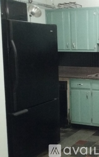 A black refrigerator in a kitchen with light blue cabinets.