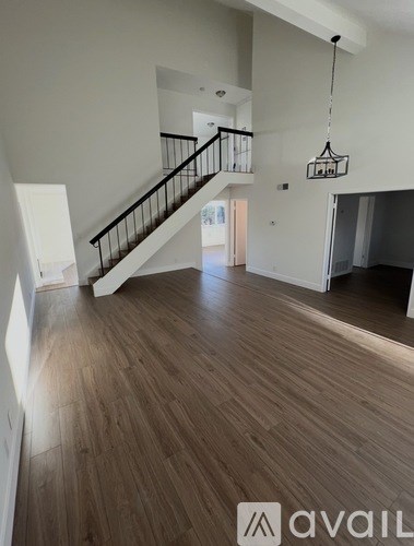 A spacious living room with wooden flooring and a staircase with a black railing.